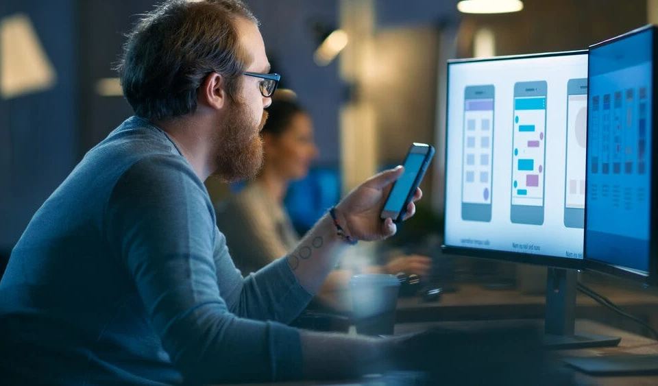 an image of a man engrossed in his phone, possibly searching for something and being targeted by an effective advertising strategy. the image conveys how businesses can use mobile marketing tactics to capture the attention of their target audience and engage them with their brand.