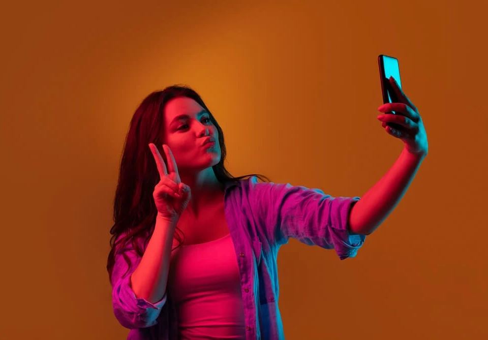 an image of a woman holding a phone, as if taking a selfie. the image is used to illustrate the importance of avoiding vanity metrics in digital marketing. vanity metrics, such as the number of likes or followers, may provide a sense of validation, but they do not necessarily translate to business success. instead, businesses should focus on meaningful metrics, such as engagement rates, conversion rates, and revenue generated. 