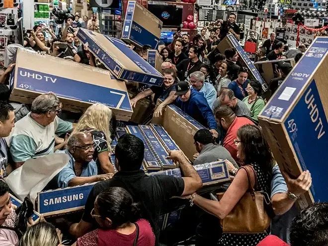 Chaotic scene of shoppers grabbing large boxed UHD TVs during a busy sale event.