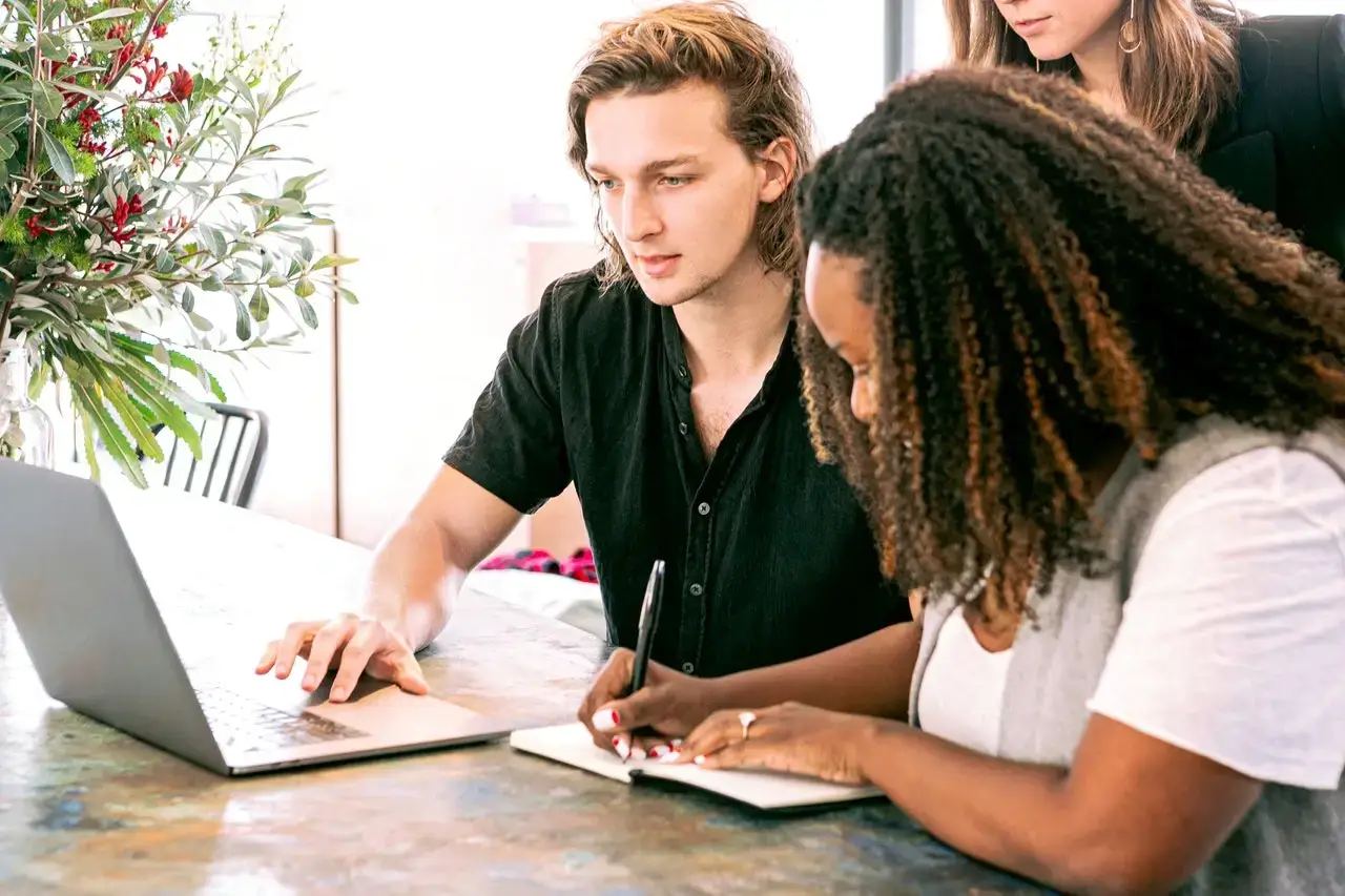 A diverse team of professionals in a modern office collaborating around a laptop, showcasing the benefits of hiring a marketing consultant