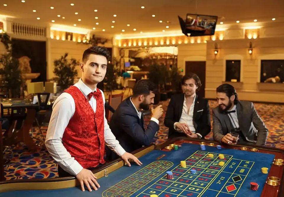 A casino dealer in a red vest stands at a roulette table as three men gamble, illustrating the illusion of control bias.