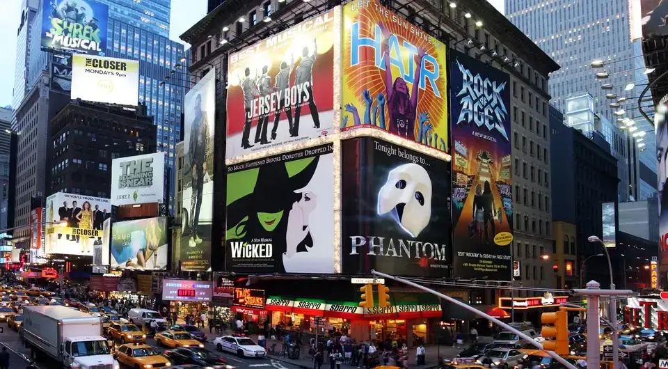 Brightly lit Broadway billboards for musicals like Wicked and Phantom, with heavy traffic below exemplify attention biases in a busy city.