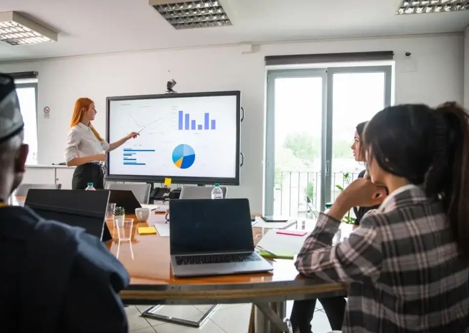A businesswoman presents data graphs on a large screen to colleagues, discussing on page SEO services strategy.