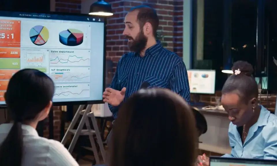 A marketing leader, perhaps a CMO defined by their role, presents business analytics on a large screen to a team.