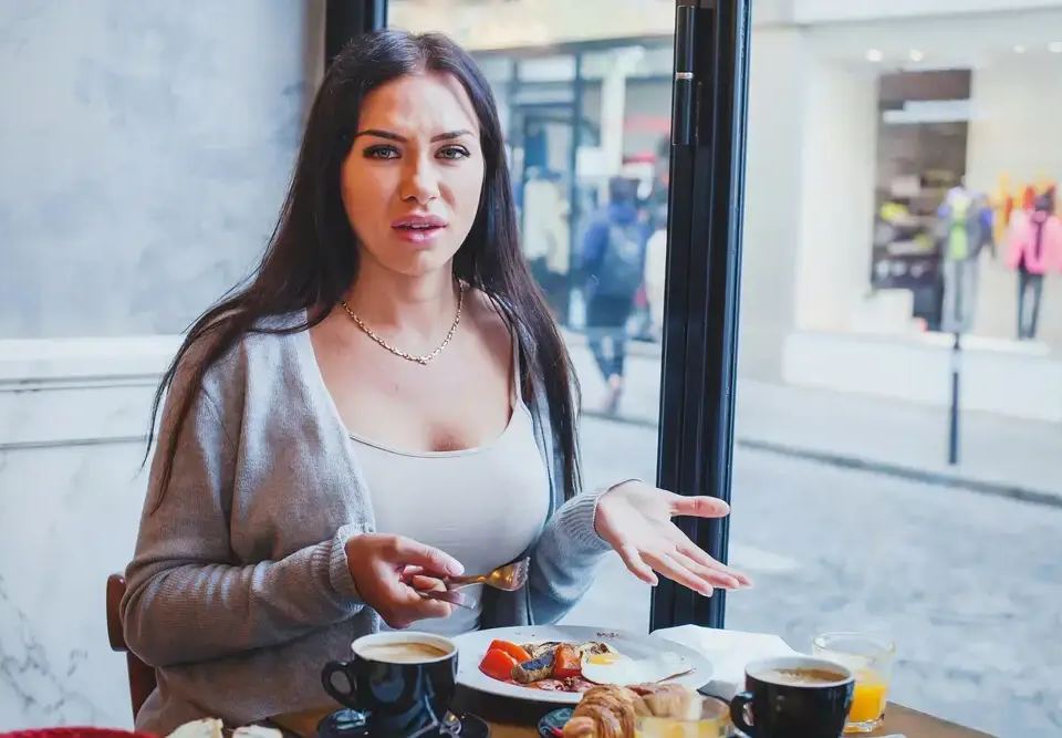 Woman looking displeased at a cafe table with breakfast, suggesting a poor customer experience that impacts how to increase customer lifetime value.