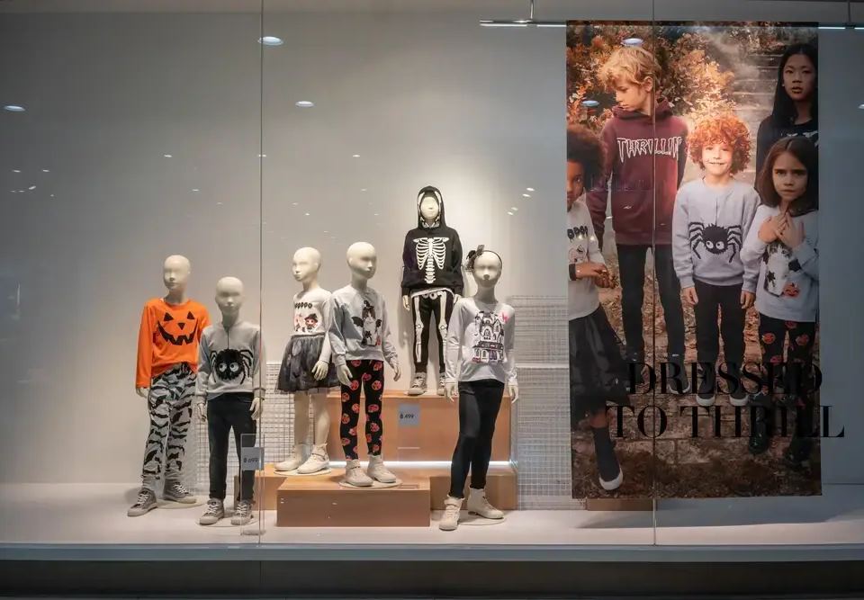 Retail window display featuring child mannequins in Halloween costumes, alongside a poster of children, illustrating a seasonal digital marketing strategy.