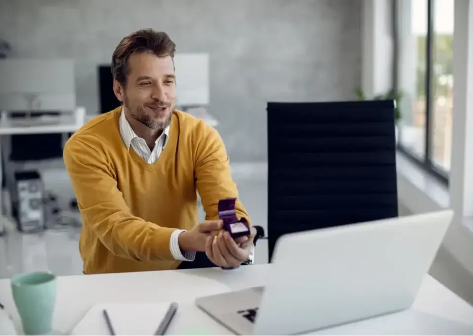 Man holding an engagement ring box during a video call, symbolizing commitment to fractional marketers.