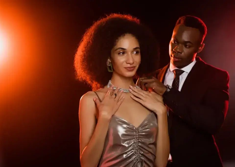 Man in suit fastening a sparkling necklace on a woman in a metallic dress, demonstrating self enhancement bias.