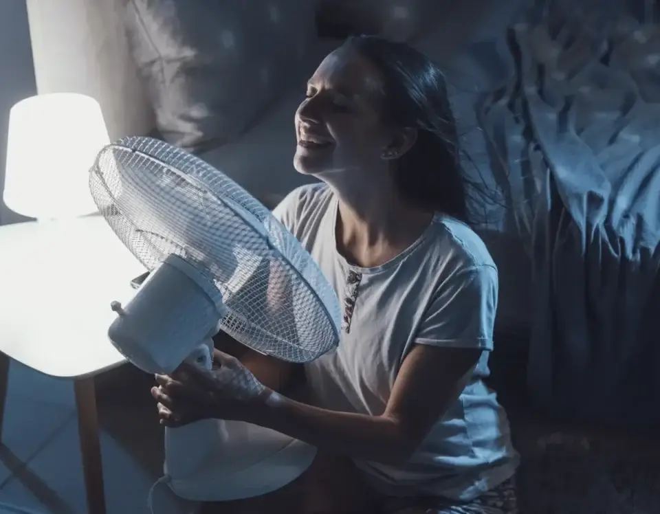 Woman smiling, enjoying cool air from a fan on a hot summer night, illustrating the impact of weather based marketing.