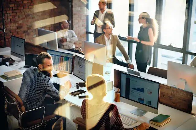 A modern office with two teams at separate tables, one representing in-house marketing, the other an agency, discussing strategies