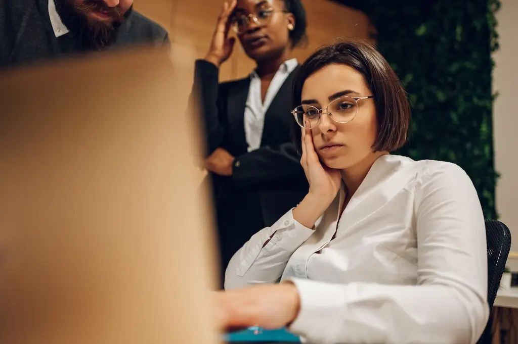 A frustrated salesperson sits at a desk, head in hands, surrounded by untouched phones and overflowing inboxes, illustrating why sales feels stuck